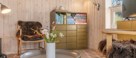Una habitación acogedora con paredes de madera, una estantería, una mesa redonda con un florero y un sillón de pelo, además de un televisor.