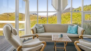 Un invernadero con sofá y sillones, ventanas amplias y vistas al paisaje.