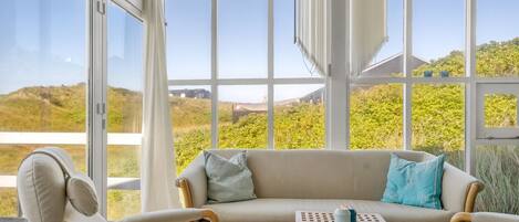A conservatory with a sofa and chairs, large windows, and a view of the landscape.