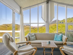 Ein Wintergarten mit einer Couch und Sesseln, großen Fenstern und Blick auf die Landschaft.