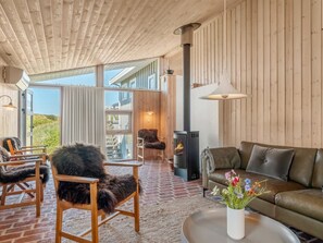 A cozy interior with a fireplace, wooden furniture, and a view through large windows. - "Elsamaria" - 400m from the sea by Interhome (Blokhus)