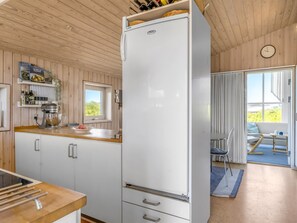 Een kleine keuken met een witte koelkast, houten kastjes, een aanrecht met een mixer en een raam.