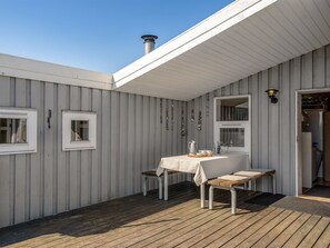 Ein überdachter Außenbereich mit Tisch, Stühlen, einem Kamin und einem Fenster.