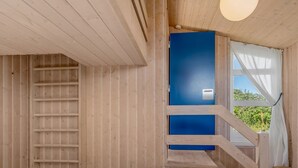 Interior de una cabaña de madera con una cama, una puerta azul y una escalera.