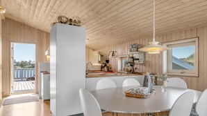 Cocina moderna con armarios blancos, una isla central y un comedor con sillas blancas.