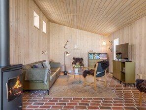 Una habitación acogedora con chimenea, un sofá, una silla, una mesita con un jarrón y una estantería.