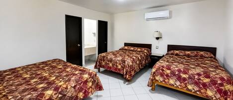 Quarto de hotel com três camas, banheiro e ar condicionado.