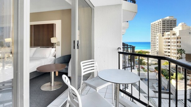 A balcony with a white table and chairs, a sofa, and a view of the ocean and buildings. - Cozy 2 Double-bed Hotel Room | Max 4 guests (Surfers Paradise)