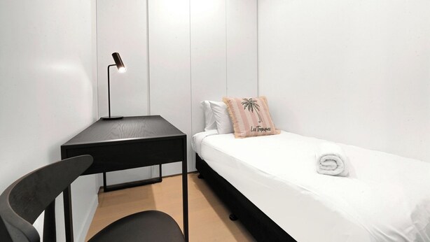A bedroom with a bed, a desk, a chair, and a wardrobe. - Casino-Side 2BR Ocean View | Walk to Beach/Tram (Broadbeach)