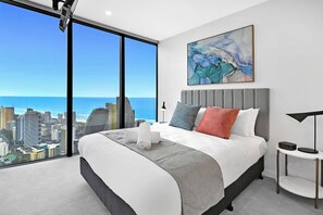 Een moderne hotelkamer met een groot bed, uitzicht op de stad, een schilderij aan de muur en een nachtkastje met een lamp.
