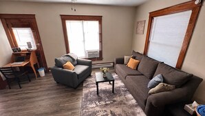 Ein Wohnzimmer mit einer Couch, einem Sessel, einem Couchtisch und einem Schreibtisch mit Stuhl.