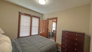 Een slaapkamer met een bed, een dressoir en een deur naar een andere kamer.