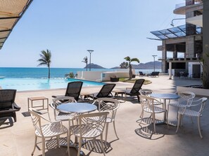 A poolside area with outdoor seating and a view of the ocean. - Family 3-Bedroom Oceanfront on the Malecón (Mazatlán)