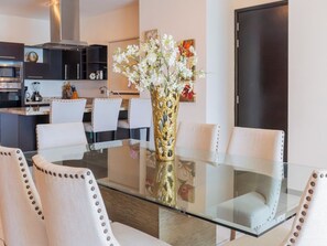 A modern dining area with a glass table, white upholstered chairs, and a decorative vase with flowers. - Family 3-Bedroom Oceanfront on the Malecón (Mazatlán)