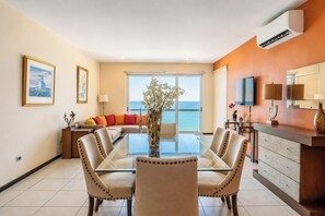 A modern living room with a glass dining table, beige sofas, and a view of the sea. - Family 3-Bedroom Oceanfront on the Malecón (Mazatlán)