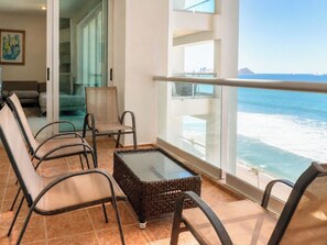 A balcony with wicker furniture, a glass table, and a view of the ocean. - Family 3-Bedroom Oceanfront on the Malecón (Mazatlán)