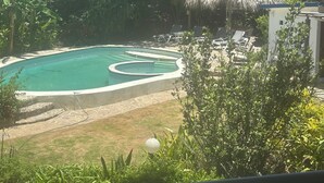 Una piscina con estructura de techo de paja, rodeada de sillas de descanso y follaje.