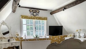 Quarto com cama, cômoda, penteadeira com espelho, televisão e janela com cortinas.