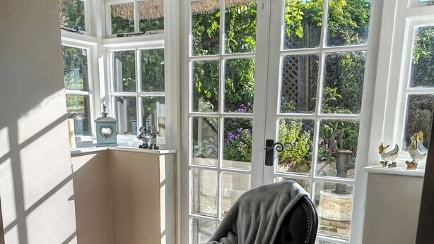 Quarto com uma poltrona de couro preta, piso de madeira e uma janela grande com vista para o verde.