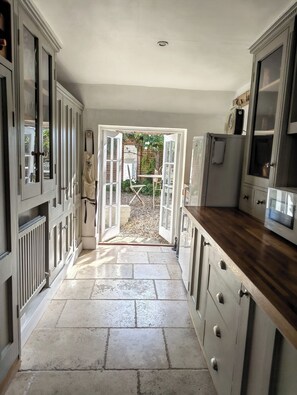 A kitchen with open doors leading to a garden, stone flooring, and wooden cabinets. - 2BR Cottage for up to 2 adults, 2 children and dogs (Wiltshire)
