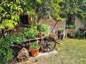 Ein rustikaler Garten mit Blumentöpfen, einem hölzernen Wagen und einer Steinmauer.