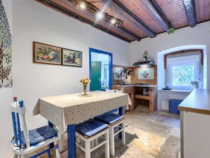 Eine Küche mit Essbereich, ausgestattet mit einem Tisch mit puntierten Tischdecke, Stühlen und einer blauen Tür.