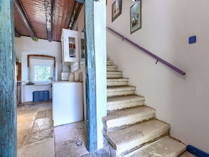 Une cuisine équipée d’un réfrigérateur, de placards et d’une fenêtre. Un escalier avec une rampe violette mène à l’étage supérieur.
