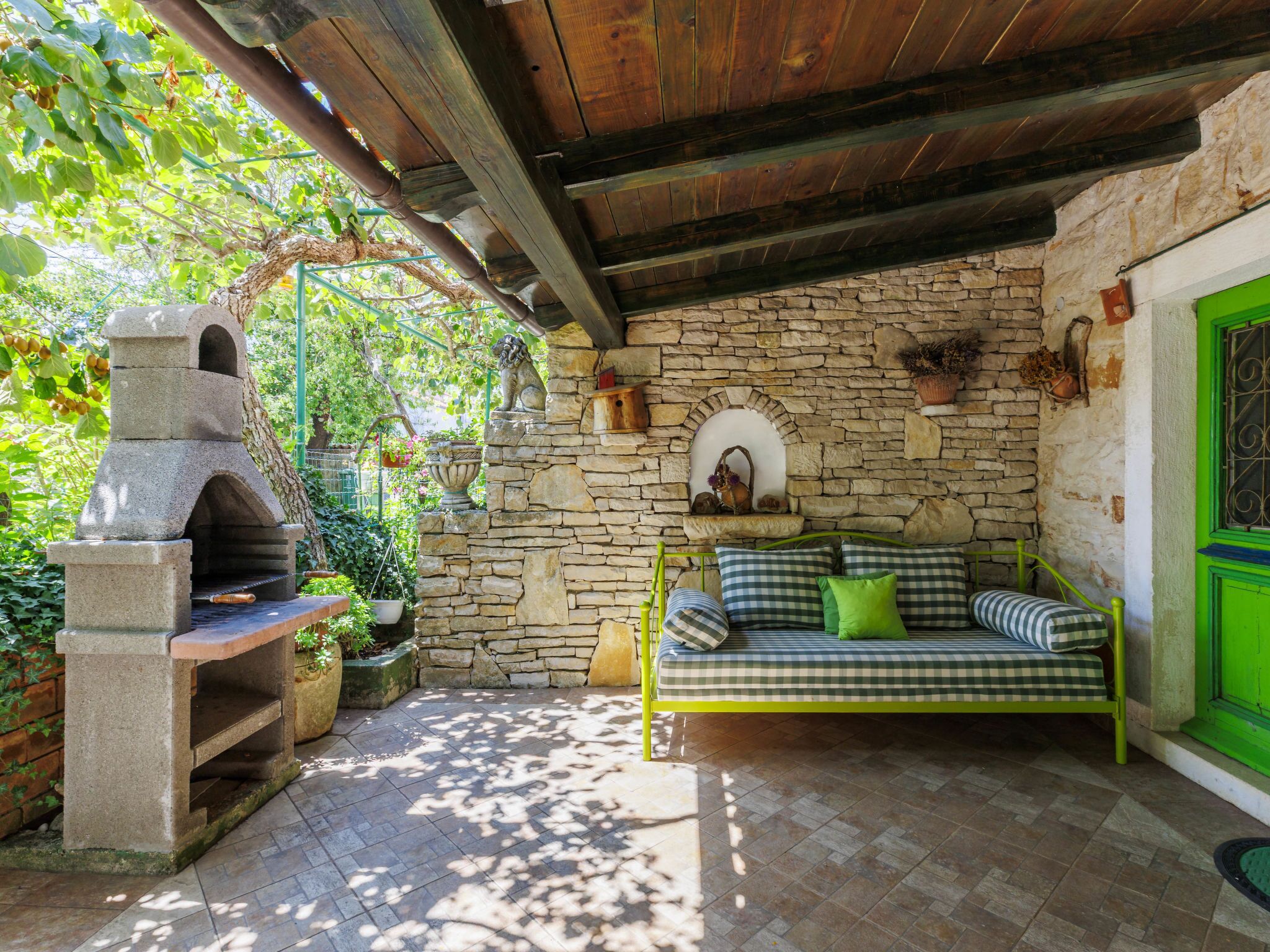 A stone-walled room with a stone oven, a green metal bed, and a stone bench.