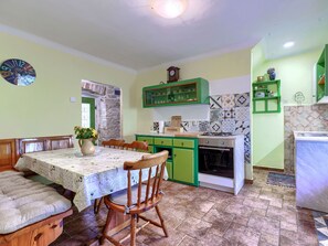 Een keuken met een eettafel, stoelen, een fornuis en groene kastjes.