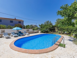 A swimming pool with a stone border, surrounded by lounge chairs and a blue umbrella. - Vacation home Helena by Interhome (Pula)