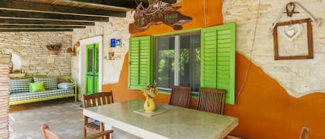 A rustic dining area with a stone wall, wooden ceiling beams, and a table with chairs.