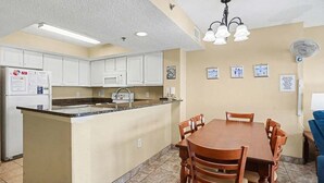 A kitchen with white cabinets, a granite countertop, a dining table with chairs, a ceiling fan, and a refrigerator. - 2BR Oceanfront View at Carolinian with Amazing  Pool (Myrtle Beach)