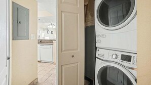 A laundry area with two stacked washing machines, a door leading to a kitchen, and a tiled floor. - 2BR Oceanfront View at Carolinian with Amazing  Pool (Myrtle Beach)