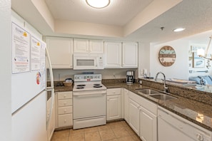 A kitchen with white cabinets, a microwave, a stove, and a sink. - 2BR Oceanfront View at Carolinian with Amazing  Pool (Myrtle Beach)