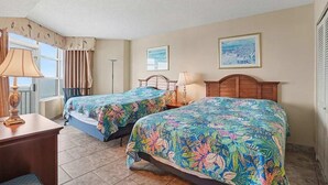 A hotel room with two beds, a desk, a window with curtains, and two wall-mounted lamps. - 2BR Oceanfront View at Carolinian with Amazing  Pool (Myrtle Beach)