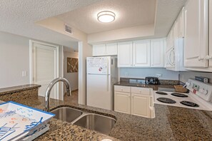 A kitchen with granite countertops, white cabinets, a stainless steel sink, a refrigerator, a toaster, and a stove. - 2BR Oceanfront View at Carolinian with Amazing  Pool (Myrtle Beach)