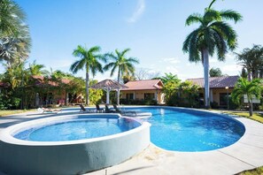 Ein Swimmingpool mit Liegestühlen, Palmen und Gebäuden mit roten Dächern.