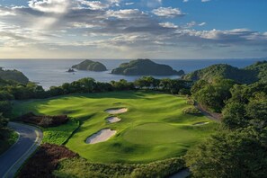 Ein Golfplatz mit Bunkern, einer Straße und Blick auf das Meer und Inseln.