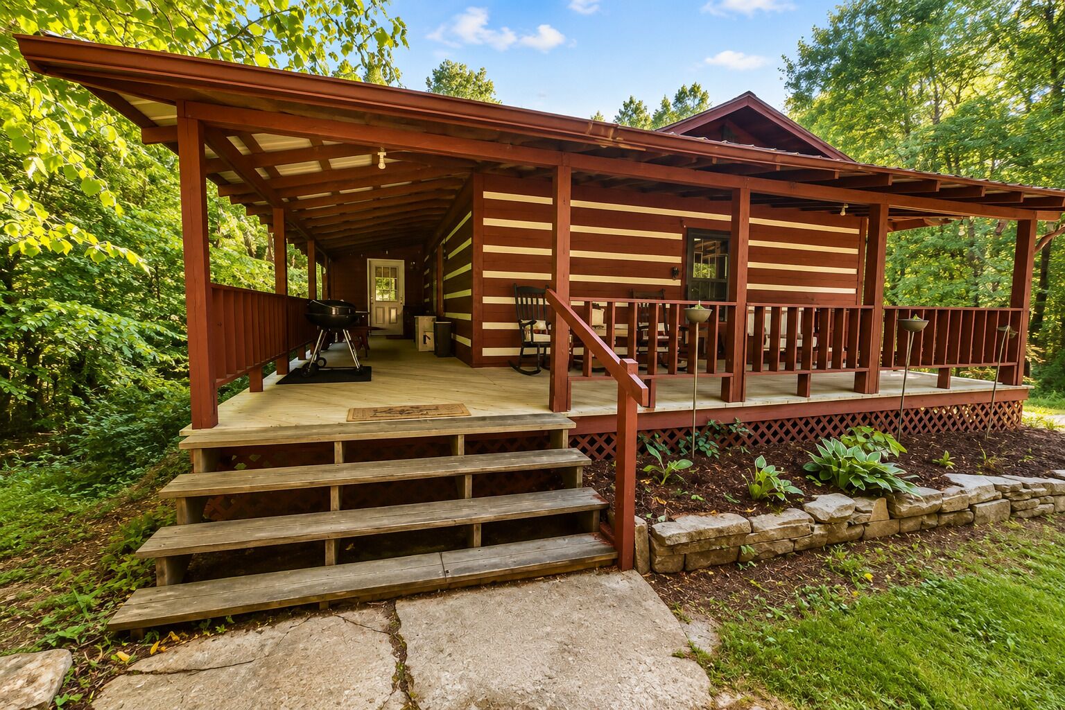A wooden cabin with a porch, steps leading up to it, and a grill outside.