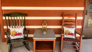 Dos mecedoras de madera con cojines a juego, una pequeña mesa de madera con un farol, y una pared de madera con tablones horizontales.