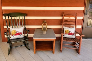 Deux fauteuils à bascule en bois, assortis de coussins, une petite table en bois avec une lanterne, et un mur en bois avec des planches disposées horizontalement.