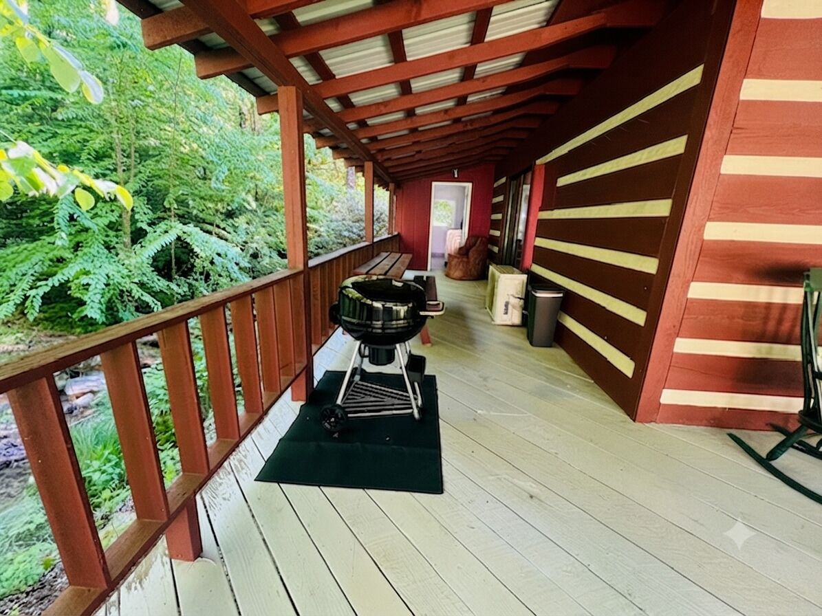 A covered outdoor area with a barbecue grill, wooden benches, and a view of a forested area.