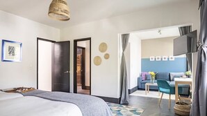 A hotel room with a bed, a desk, a chair, a television, and a view into the living area.