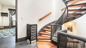 A spiral staircase with wooden steps and a black railing, leading to an upper floor.