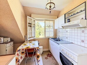 Eine Küche mit Fenster, Spüle, Herd und einem Tisch mit Blumenmuster bedeckter Tischdecke.