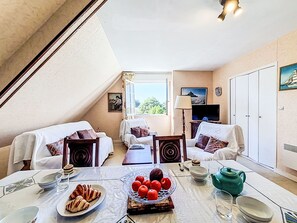 Ein gemütliches Zimmer mit zwei weißen Sofas, einem Esstisch mit Frühstück, einem Fernseher und einem Kleiderschrank.