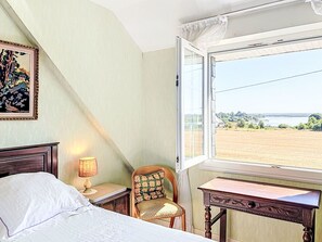 Ein Schlafzimmer mit einem Bett, einem Sessel, einem Schreibtisch und einem Fenster mit Blick auf ein Feld.