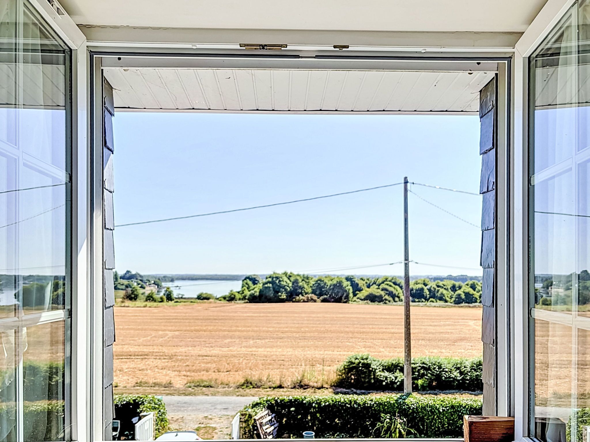 A view through an open door with a clear sky, a field, and a distant body of water.