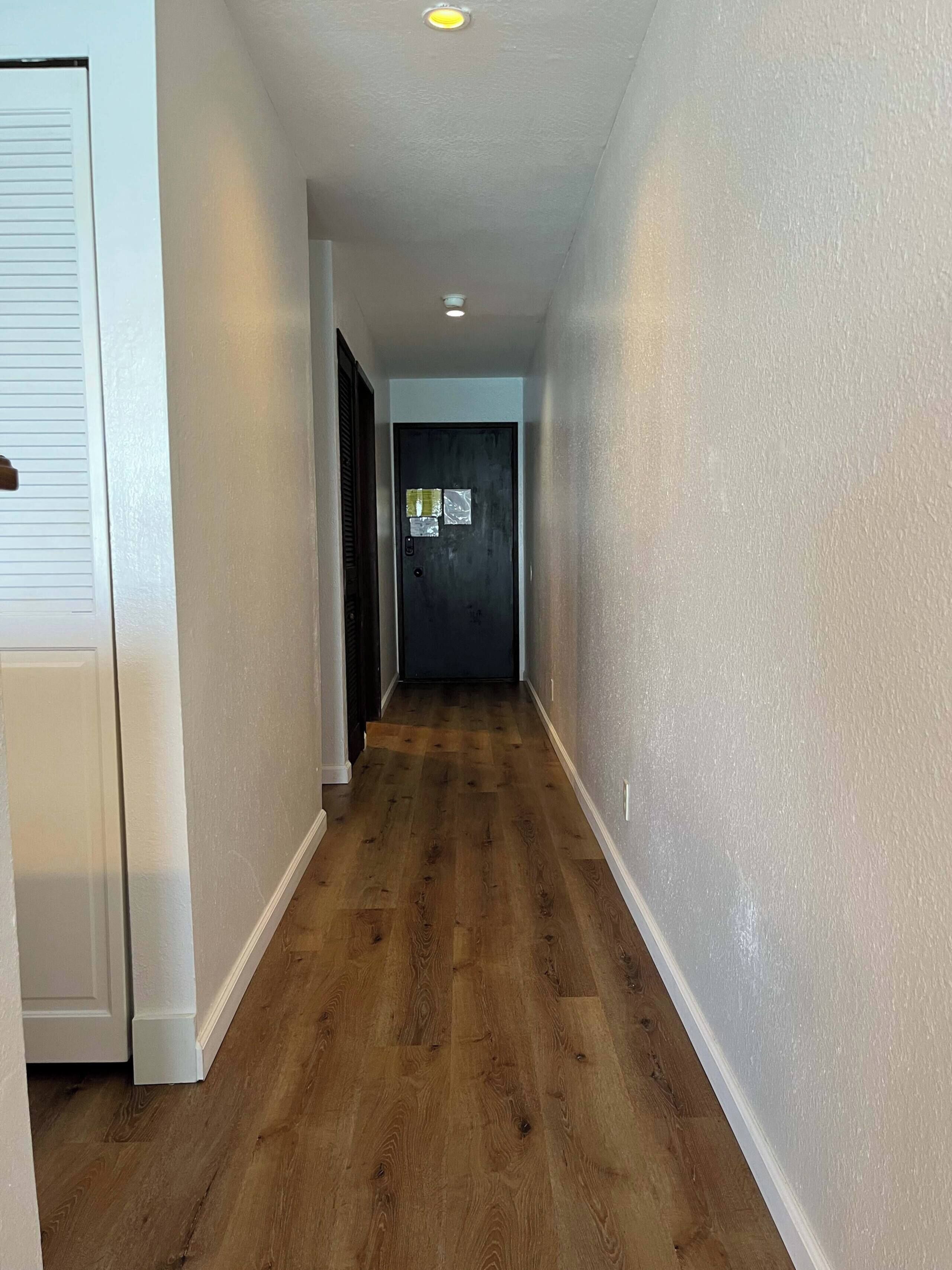 Un couloir doté d’un plancher en bois, de murs blancs et d’une porte au fond.