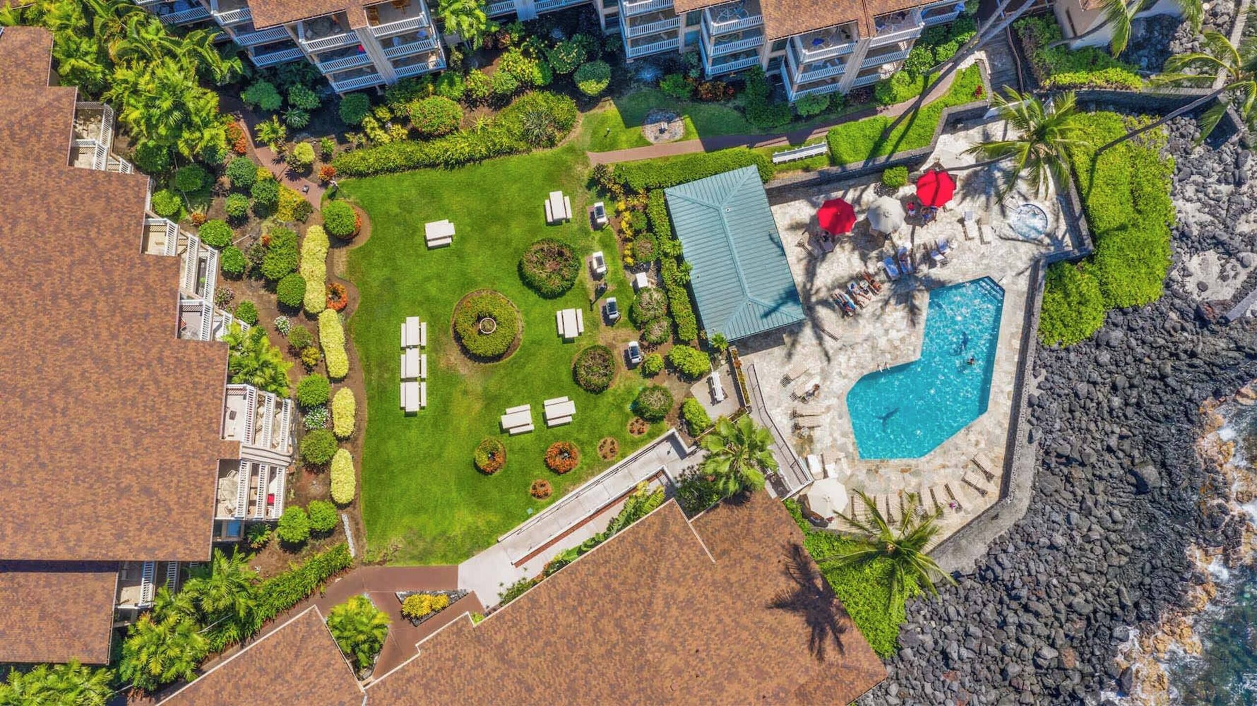 Vue aérienne d’un complexe hôtelier doté d’une piscine, de chaises longues et d’une pelouse bien entretenue.